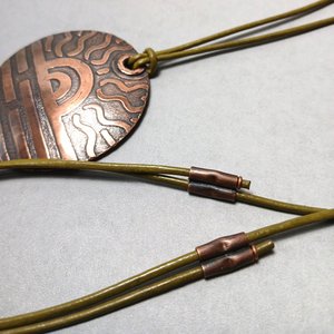 Close up of sliding copper tubes to adjust cord length on etched copper pendant.