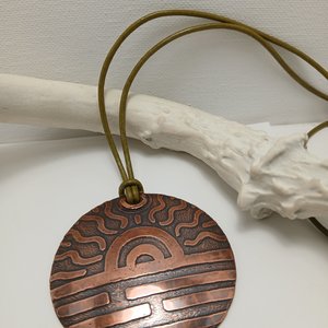 Large 2.25" copper disk pendant with etched sun design. Hung on absinthe green leather cord. Displayed against white antler on white background.