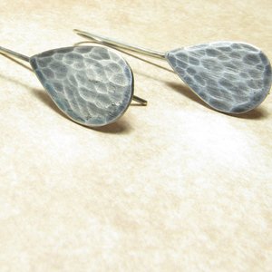 Classic tear drop earrings in hammered silver. Displayed on beige background.