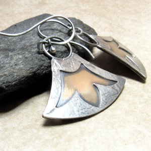 Two tone earrings by Mocahete in mixed metals with cut out design of Egyptian lotus. Displayed against black rock on neutral background.