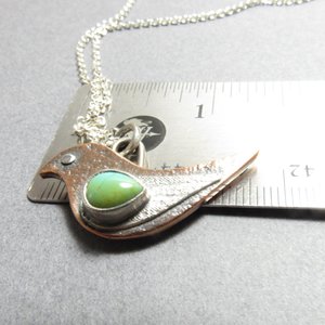 Mixed metal bird pendant necklace with turquoise displayed against ruler showing size at apx. 1.33" from beak to tail.