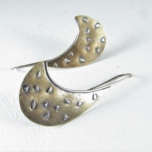 A pair of silver and bronze earrings with a curved shape and a textured surface. The earrings have a oxidized finish and are a unique and stylish accessory.