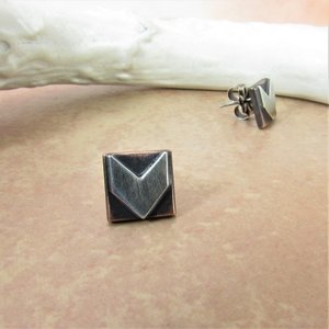 Sterling silver and copper stud earrings with a geometric arrow design. The earrings are square shaped with a pointed arrow in the center. Displayed against antler on sand color background.