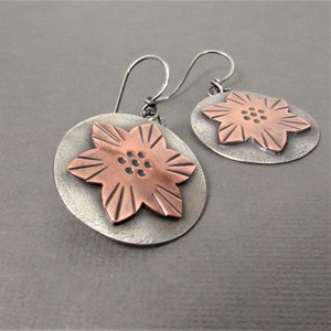 Handmade Sterling silver earrings with copper flower accents. The flowers have  texture and pattern  and are set against a smooth, silver background. SS earwires, 1.5" tall 1" wide. Lightweight. Displayed on grey background.