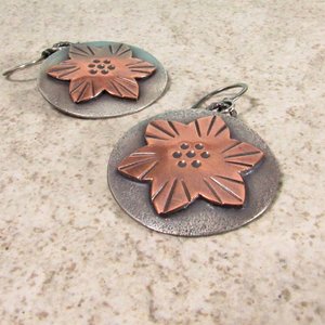 Mixed metal earrings feature a flower design in copper and sterling silver. They are a layered design, lightweight and measure 1.5" tall and 1" wide. The earrings are handcrafted and exceptional quality. Displayed on sand color background.