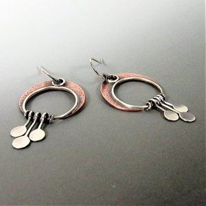 A pair of silver and copper  crescent moon earrings with a circular design and dangling silver discs. 2 inches tall and 1 " wide. Displayed on grey background.