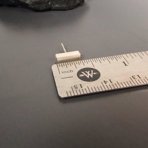 A sterling silver bar earring measuring approximately 1/2 inch in length. The earring is shown next to a ruler for size reference.