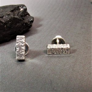 Front view of a pair of sterling silver stud earrings with a textured rectangular design. The earrings have a post back. Displayed on grey background with dark rock.