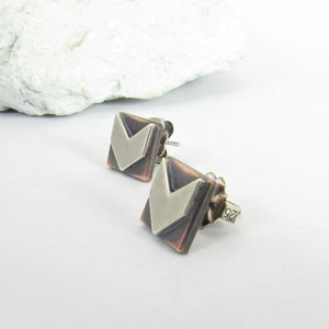 Side view of a pair of silver and copper earrings with a geometric arrow design. The earrings are square shaped with a silver arrow pointing down in the center of each earring. SS clutch backs included.