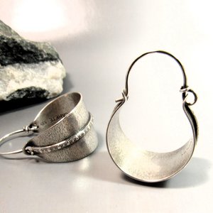 Sterling silver hoop earrings basket style fancied up with a strip of patterned  silver wire against textured argentium silver. A perfect sterling silver hoop earring for every occasion!  Oxidized, polished, finished with sterling ear wires. 1.25" or 3.1cm tall,  7/8" or 2.22cm wide. Displayed on neutral background with black and white rock.