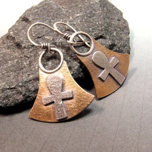 Mixed metal, bronze and silver ankh earrings. Body of earring shaped similar to the egyptian lotus motif with ankh on the front, suspended by silver ring and ear wires. 1.5" tall and 1" wide at widest point.  Displayed against black rock on grey background.