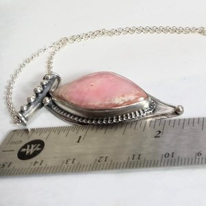 Soft elegance meets artisan craftsmanship in this one of a kind handcrafted pendant featuring a beautifully pastel pink opal set in textured Argentium® sterling silver. The unique, petal-shaped stone in a petal shaped setting radiates gentle warmth in a soothing blush hue—perfect for those who adore subtle statement pieces with soulful charm. 2.25" long x 7/8" wide.