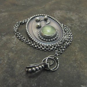 Sterling silver and green prehnite cabochon paisley necklace on dark stone colored tile background with chain coiled around pendant and clasp in foreground.