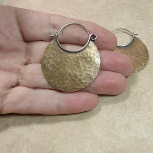 Photo in hand of large mixed metal hammered hoop earrings.