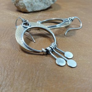 Side view of crescent moon dangle earrings with paddle fringe by Mocahete. Brown background.