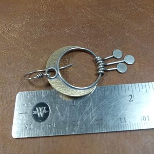 Bronze and Argentium silver crescent moon dangle earrings against ruler on brown background.