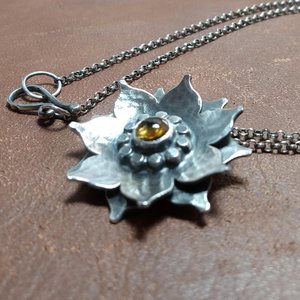 Close up of argentium lotus flower pendant with citrine on leather background.