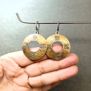Mixed metal, bronze and silver coin style earrings hanging from stand against fingers to show detail