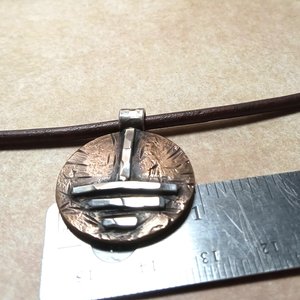 Grounding symbol pendant against ruler to show size.