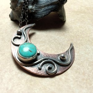 Copper and silver moon pendant set with turquoise against black shell on beige background.