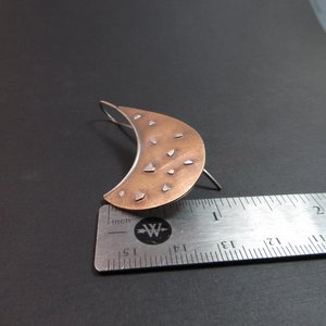 Avant garde style bronze and sterling silver earrings by Mocahete against ruler and black background.