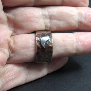 Bird ring on finger, hammered copper with silver bird on dark background.