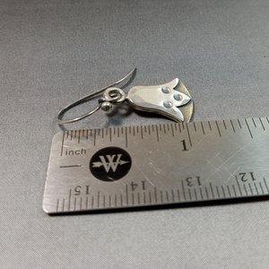 Mixed metal lotus earrings against ruler on grey background