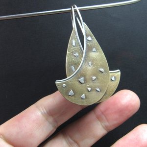Mixed metal, bronze and sterling silver earrings with an avant garde spirit, photo against fingers on dark background.