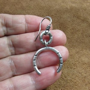 One of a pair of argentium open hoop earrings. Displayed in hand on brown leather.