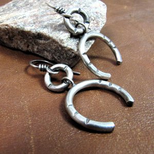Side view of contemporary sterling silver earrings crafted from Argentium have lovely swingy movement. The double open hoop design allows for them to articulate. Lightweight and comfortable  at only 5 grams per earring. 1.75” long and 7/8” at widest point. Displayed on brown leather and rock.