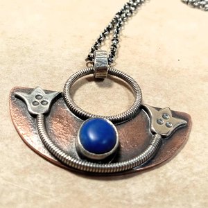 Handcrafted mixed metal lotus pendant in argentium silver and copper with lapis lazuli cabochon. Displayed on neutral background.