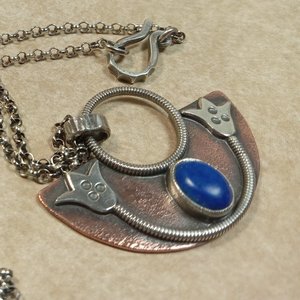 Up close photo to show details of Handcrafted mixed metal lotus pendant in argentium silver and copper with lapis lazuli cabochon. Displayed on neutral background.