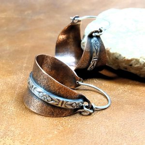 Close up of ear wire detail of Two tone mixed metal basket shaped hoop earrings in copper and sterling silver. The textured copper hoops are encircled with a floral pattern sterling silver wire and SS ear wires. Displayed on light brown back ground with white rock.