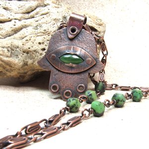 Up close photo of handcrafted copper, jade and chrysoprase hamsa pendant necklace. 2" tall x 1.5" wide, 24.5" copper scroll chain with 3 faceted chrysoprase beads on each side. All riveted design. Displayed against rock on neutral background.