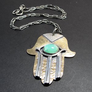 Close up of hamsa pendant necklace showing chain detail. Displayed on dark grey background