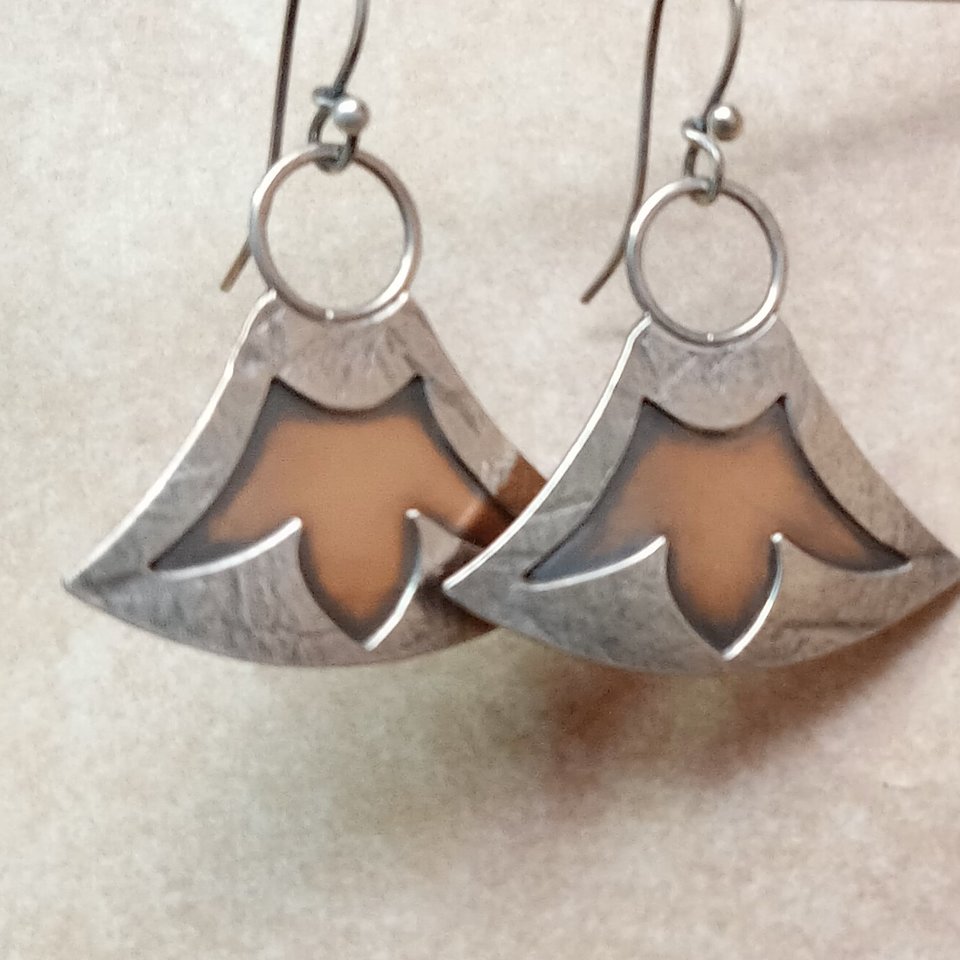 Two tone mixed metal earrings in bronze and sterling silver with a cut out lotus design. Displayed hanging from stand against neutral background.