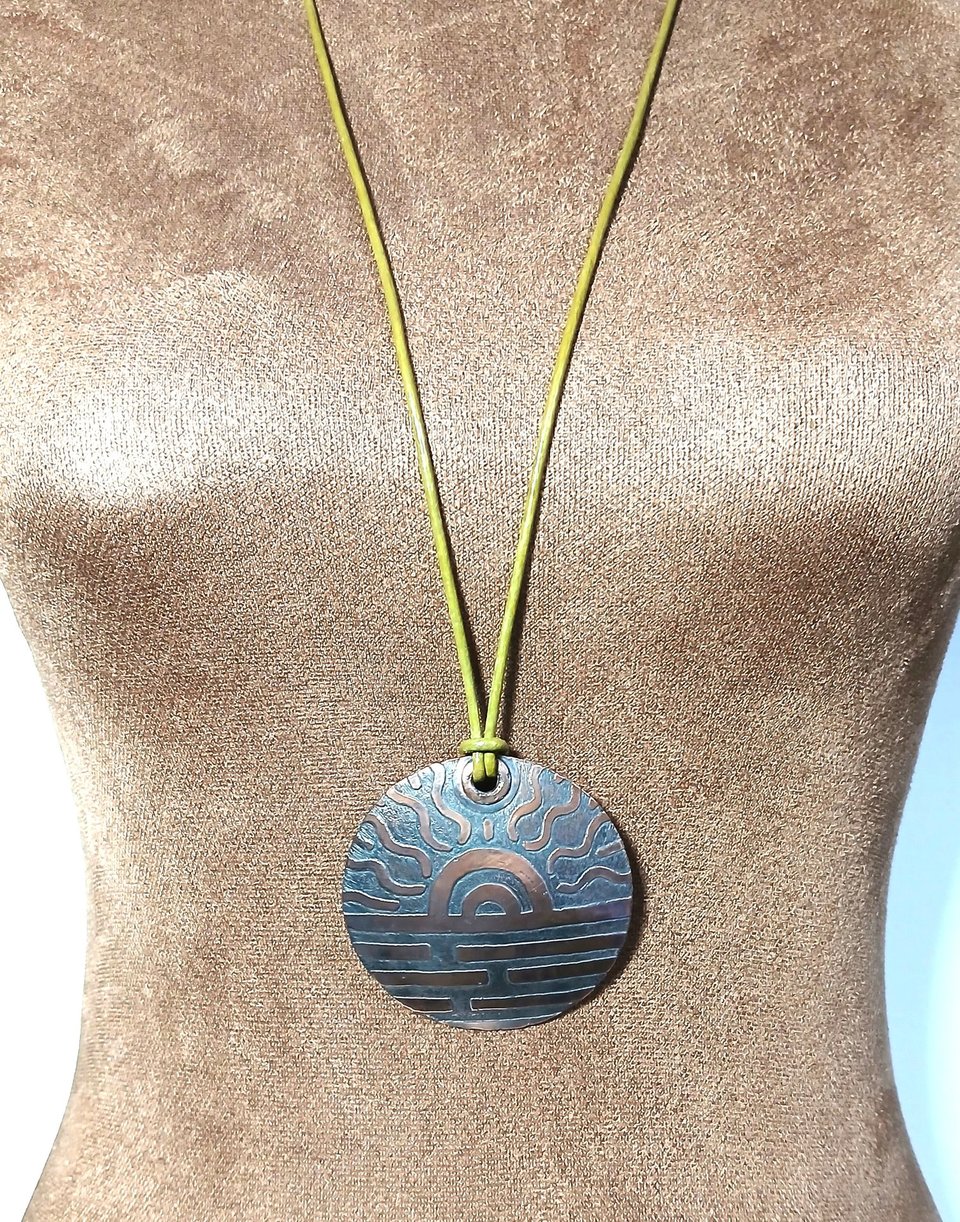 Large copper disk pendant hung on leather cord displayed on mannequin.