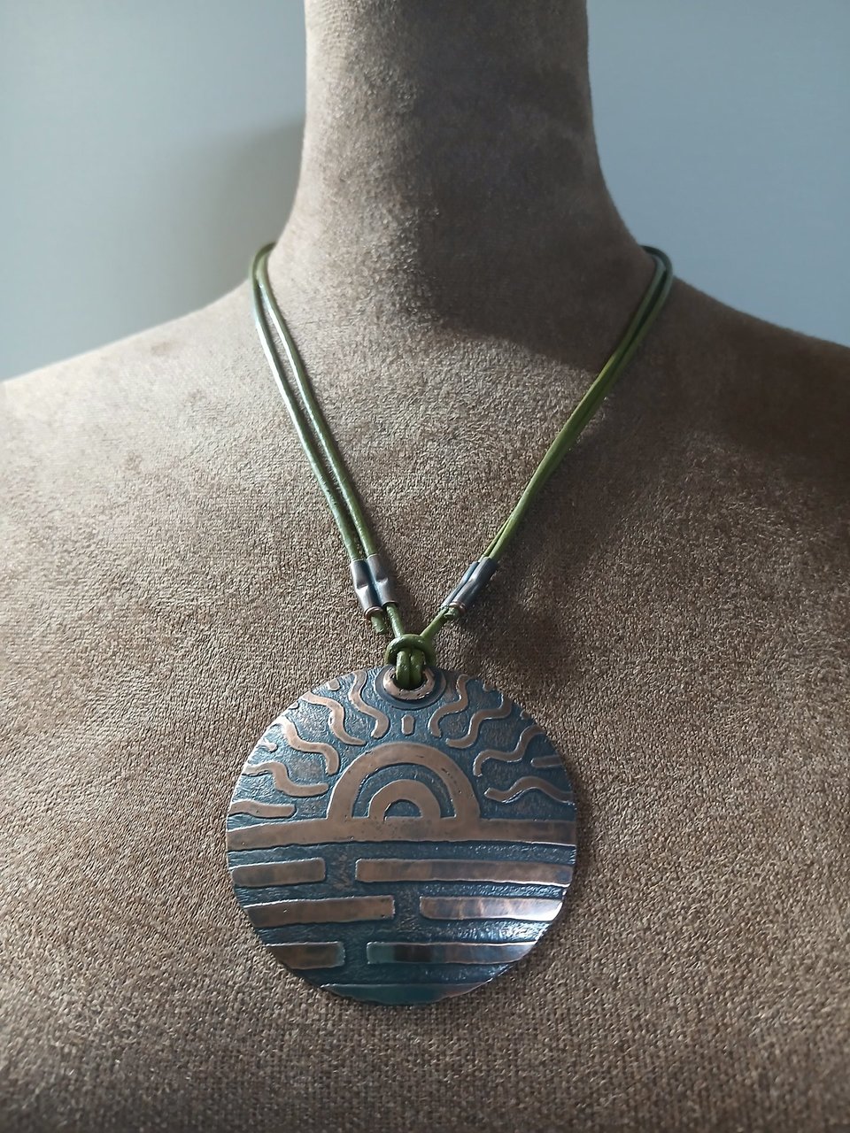 Large copper pendant with adjustable leather cord displayed on mannequin.