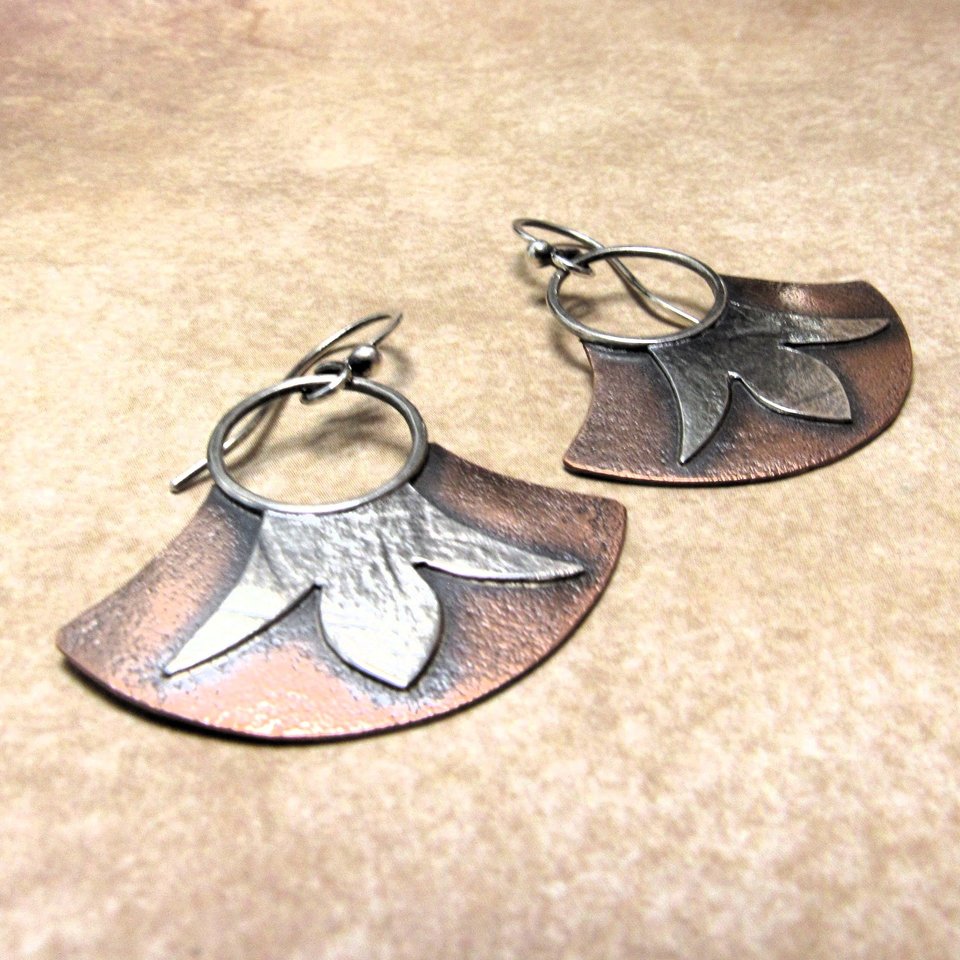 Mixed metal dangle earrings with copper and silver, floral detail, displayed against sand color background.