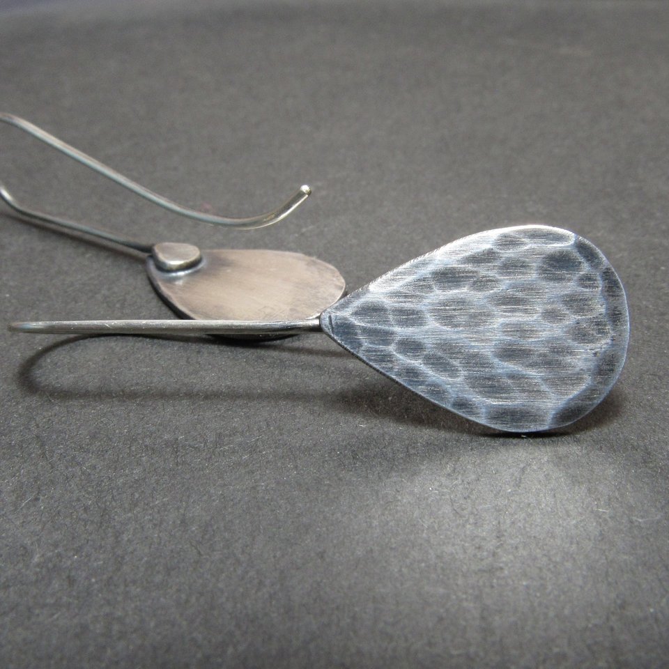 Hammered argentium silver teardrop earrings one shows reverse side. Displayed on grey background.