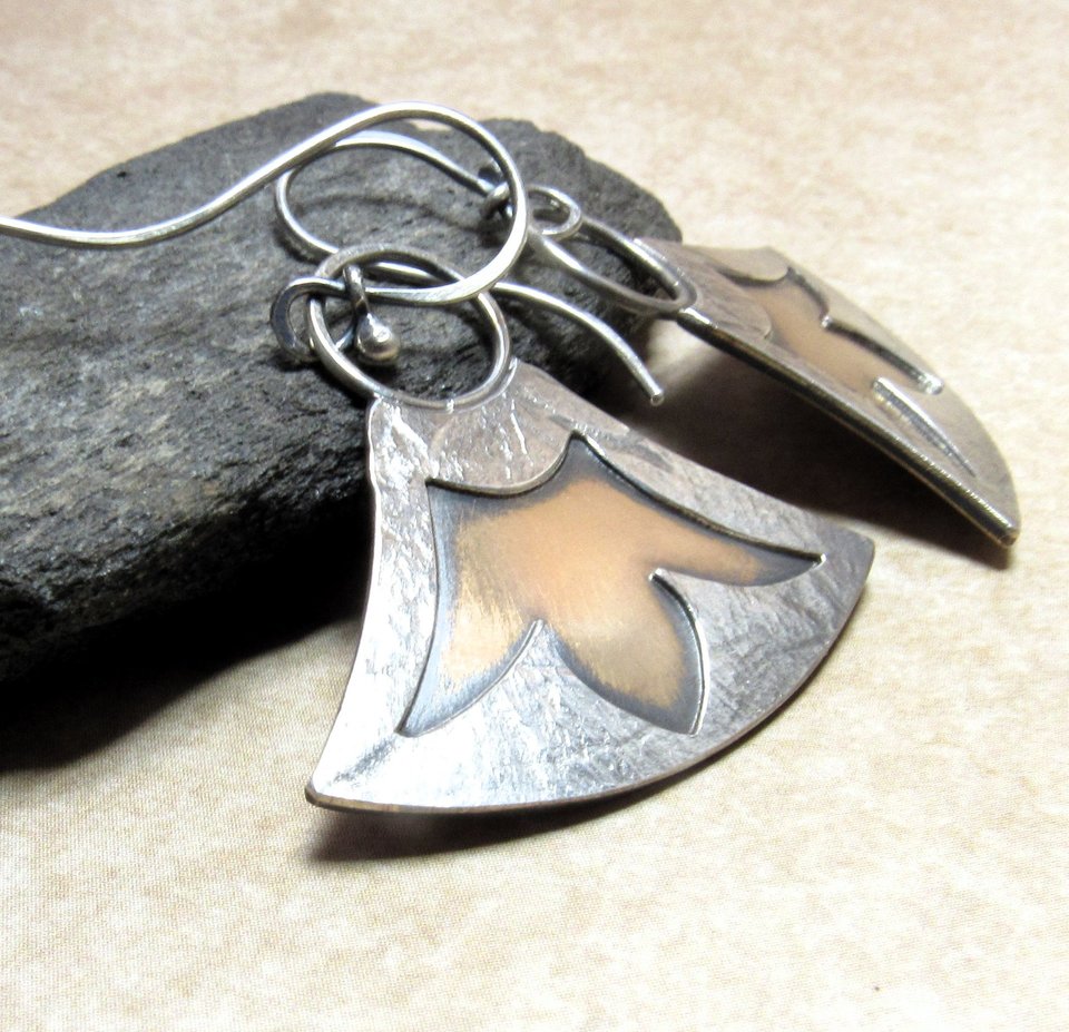 Two tone earrings by Mocahete in mixed metals with cut out design of Egyptian lotus. Displayed against black rock on neutral background.