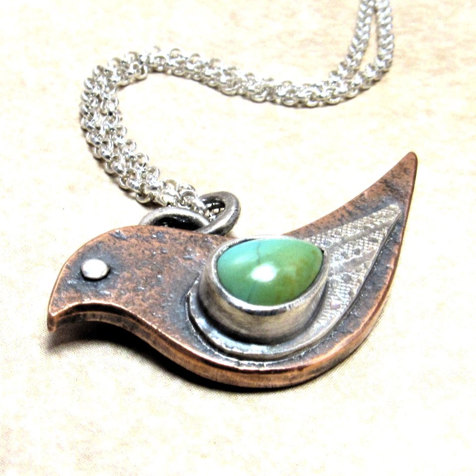 Mixed metal, copper and silver bird pendant with a turquoise cabochon set on the wing. 18" sterling silver chain and findings. Displayed on neutral background