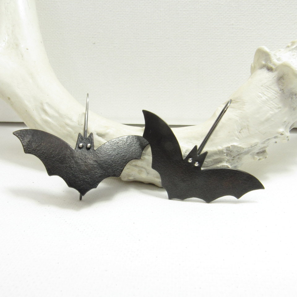  A  pair of bat earrings with oxidized copper body, sterling silver eyes and ear wires. Displayed on white antler and background.