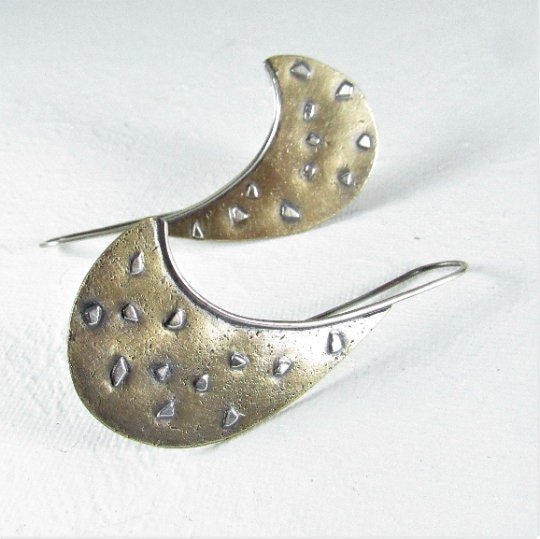A pair of silver and bronze earrings with a curved shape and a textured surface. The earrings have a oxidized finish and are a unique and stylish accessory.