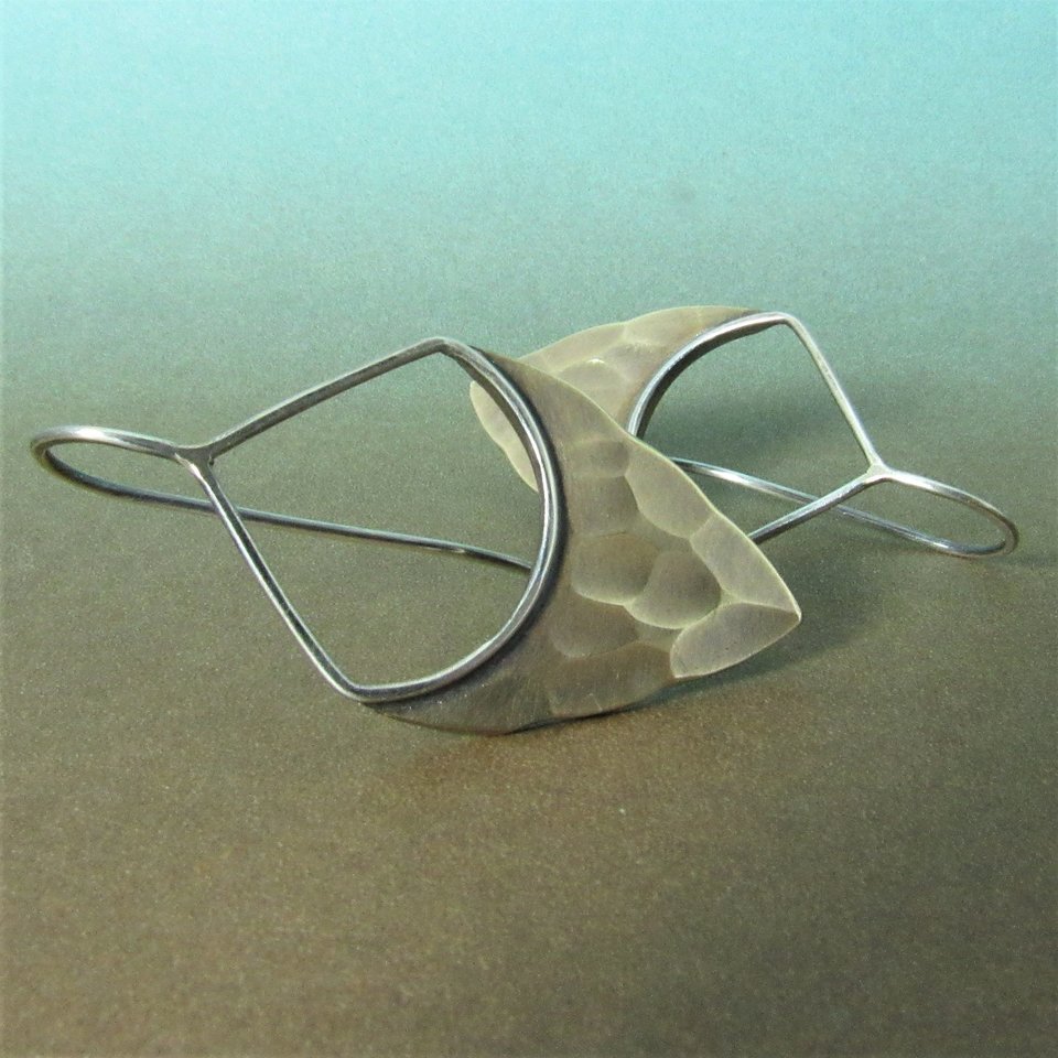 Striking, handcrafted sterling silver and bronze earrings have a two tone geometric design. Hammered for a knapped arrowhead appearance , oxidized and polished. Designed with a sterling silver fixed ear wire which holds them close to flatter your face. 1-5/8" (4.12cm) tall and 7/8" (2.2cm) wide.  Displayed against blue and brown background.