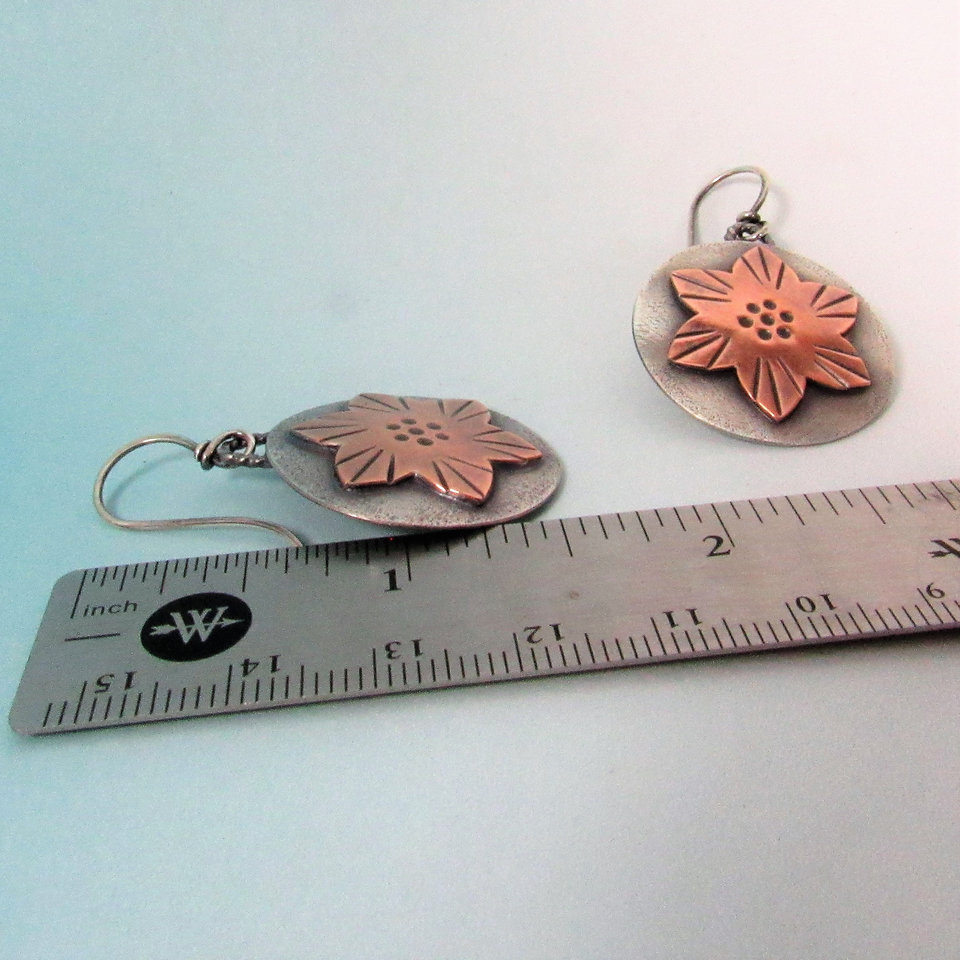 A pair of handcrafted sterling silver earrings with copper flower accents. The earrings are 1 inch in diameter and have a simple wire hook closure. Lightweight. Displayed against ruler. 1.5" tall.