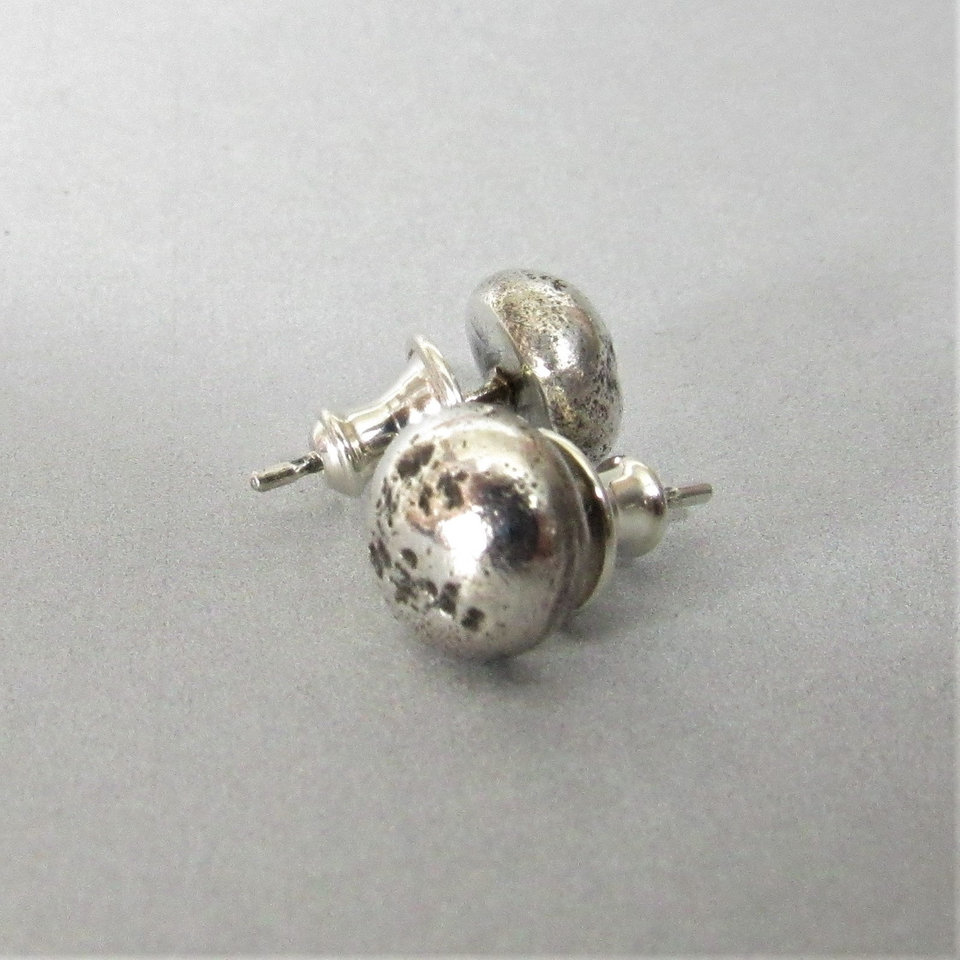 A rustic pair of silver stud earrings with a textured finish. The earrings are round and have a post back.