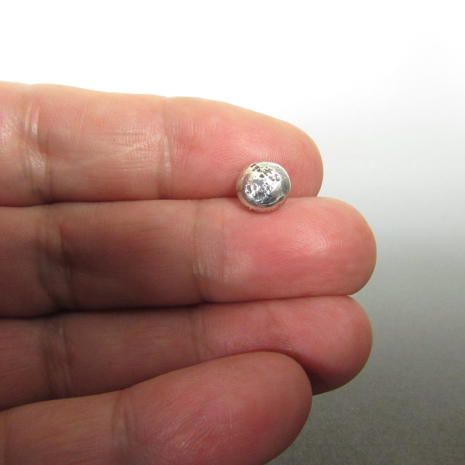 Small, silver, round sterling silver nugget stud earrings with a textured surface. Photo in hand.