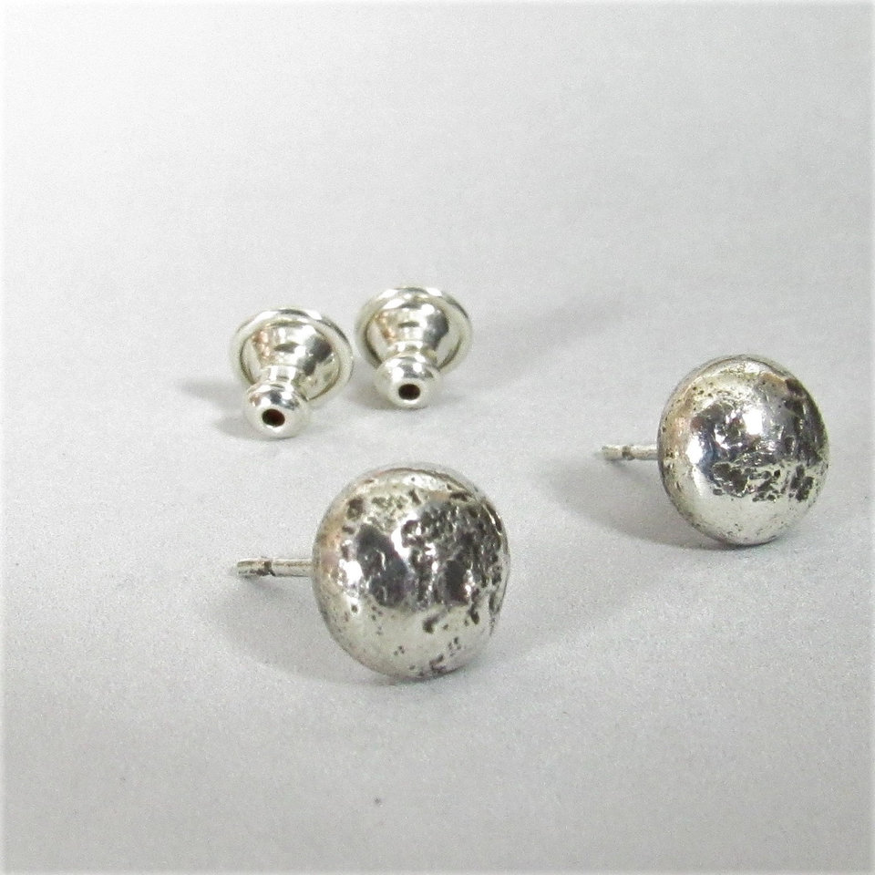 A pair of silver stud earrings with textured round tops. The earrings have a post and ss clutches.