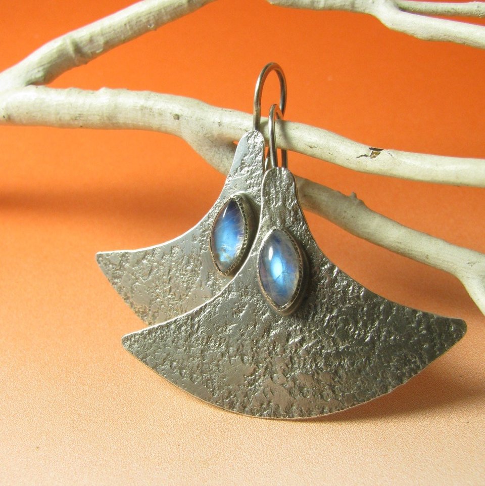 Large, futuristic argentium sterling silver and rainbow moonstone earrings with a touch of rusticity. Unusual and unique earrings that are modern with hints of the past. 1.5 inches tall x 1.75 inches wide. Displayed against dark orange background and white twig.